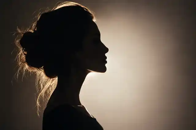 Ritratto in controluce di una donna di profilo, con luce ambrata sui capelli